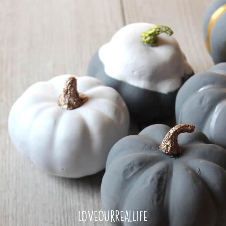 Gray and white faux craft pumpkins with glitter stems on wooden table.