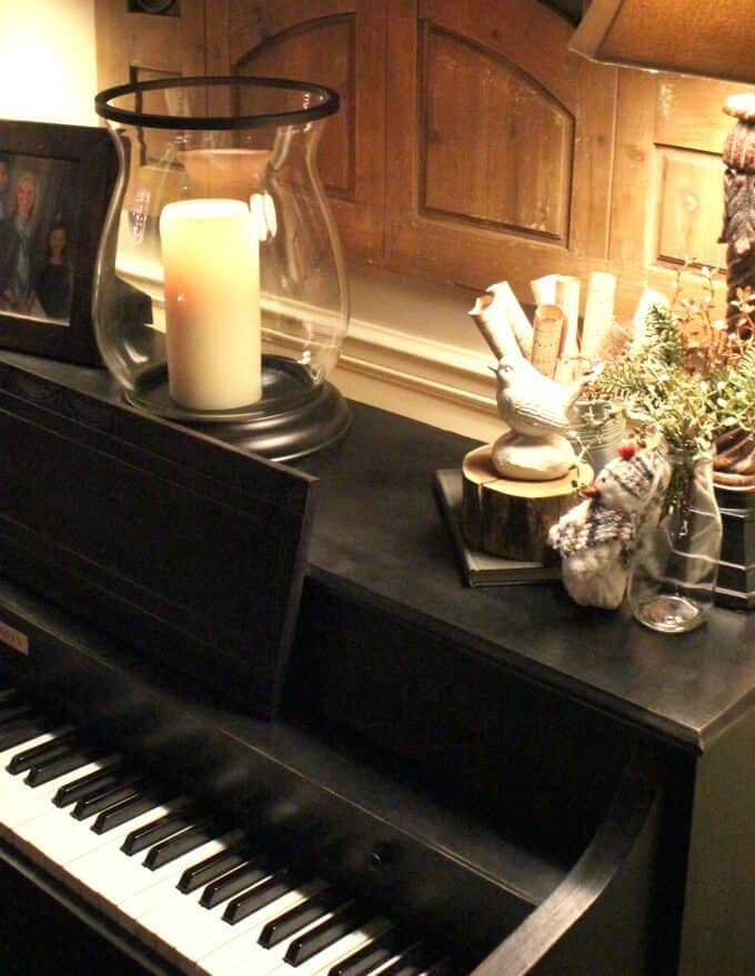 Black, chalk-painted piano with large candle and Christmas decor on top.