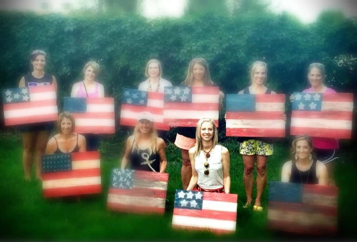 Nine women holding rustic wooden American flags.