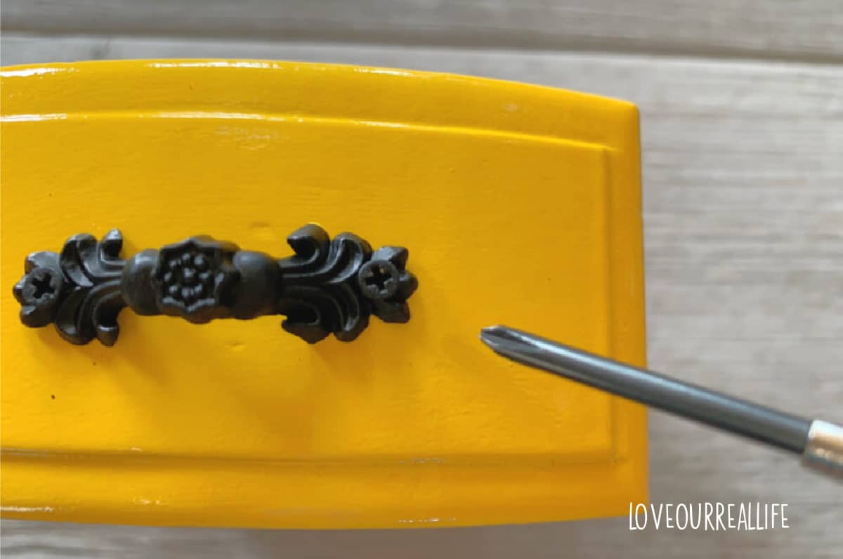 Using small screwdriver to reattach black hardware to yellow jewelry box drawer.
