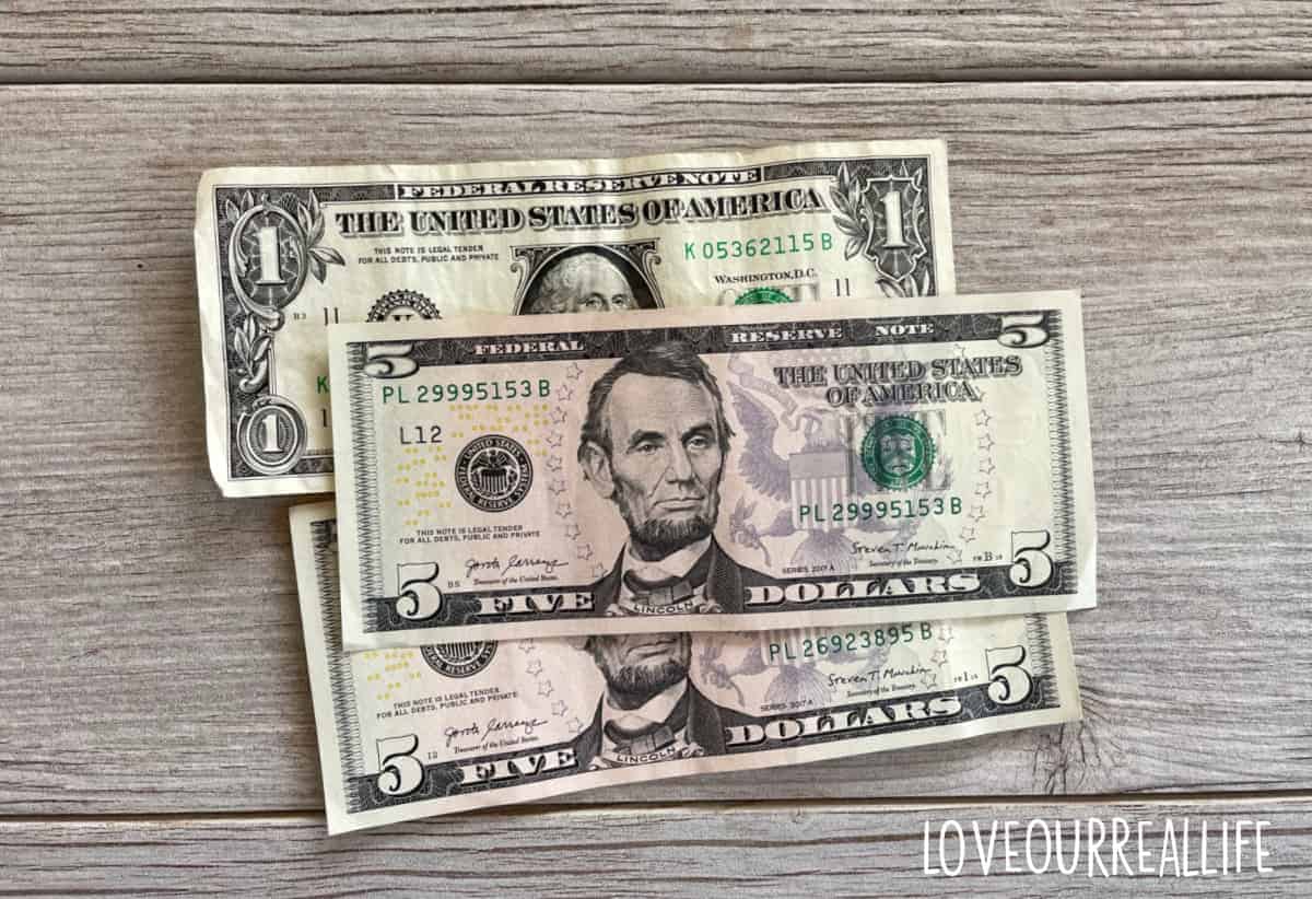 Two five-dollar bills and a one-dollar bill on gray wood.