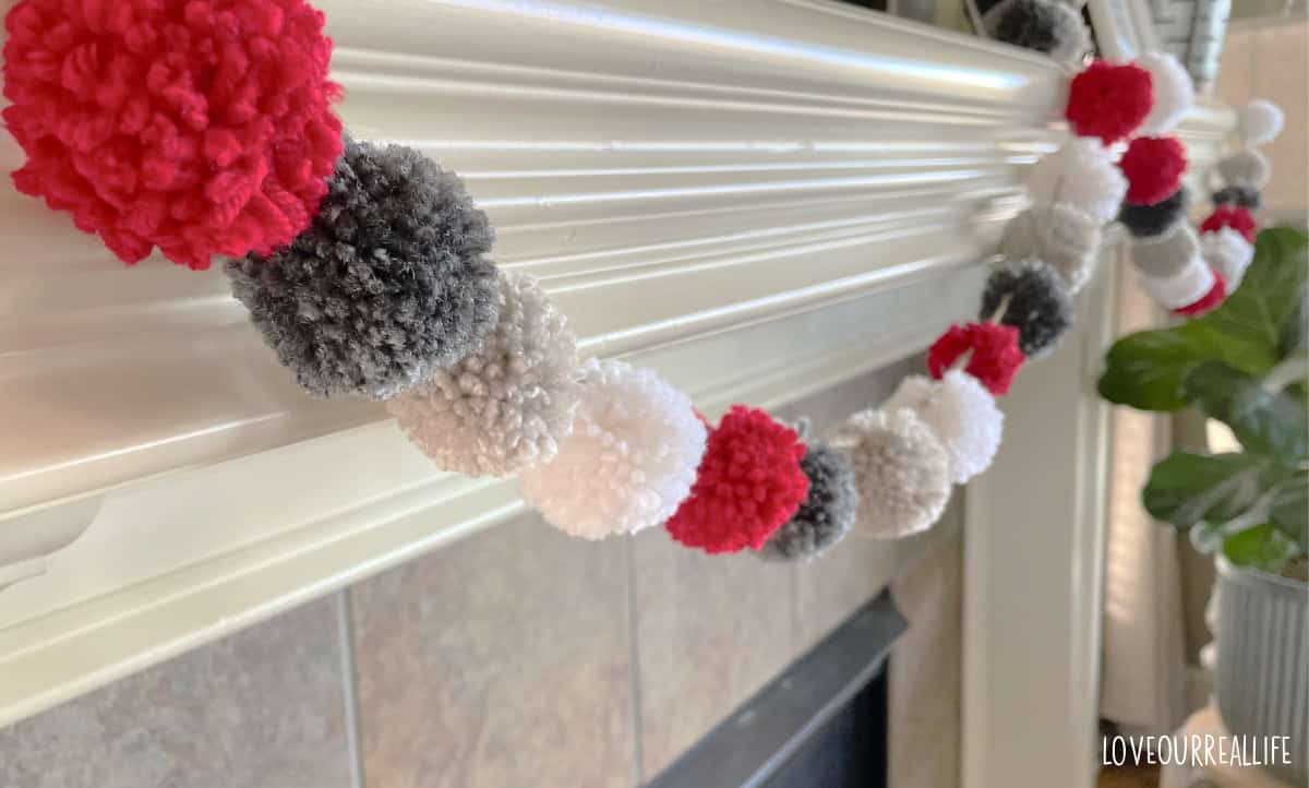 Four colors of yarn used for pom pom garland, hanging on mantel.