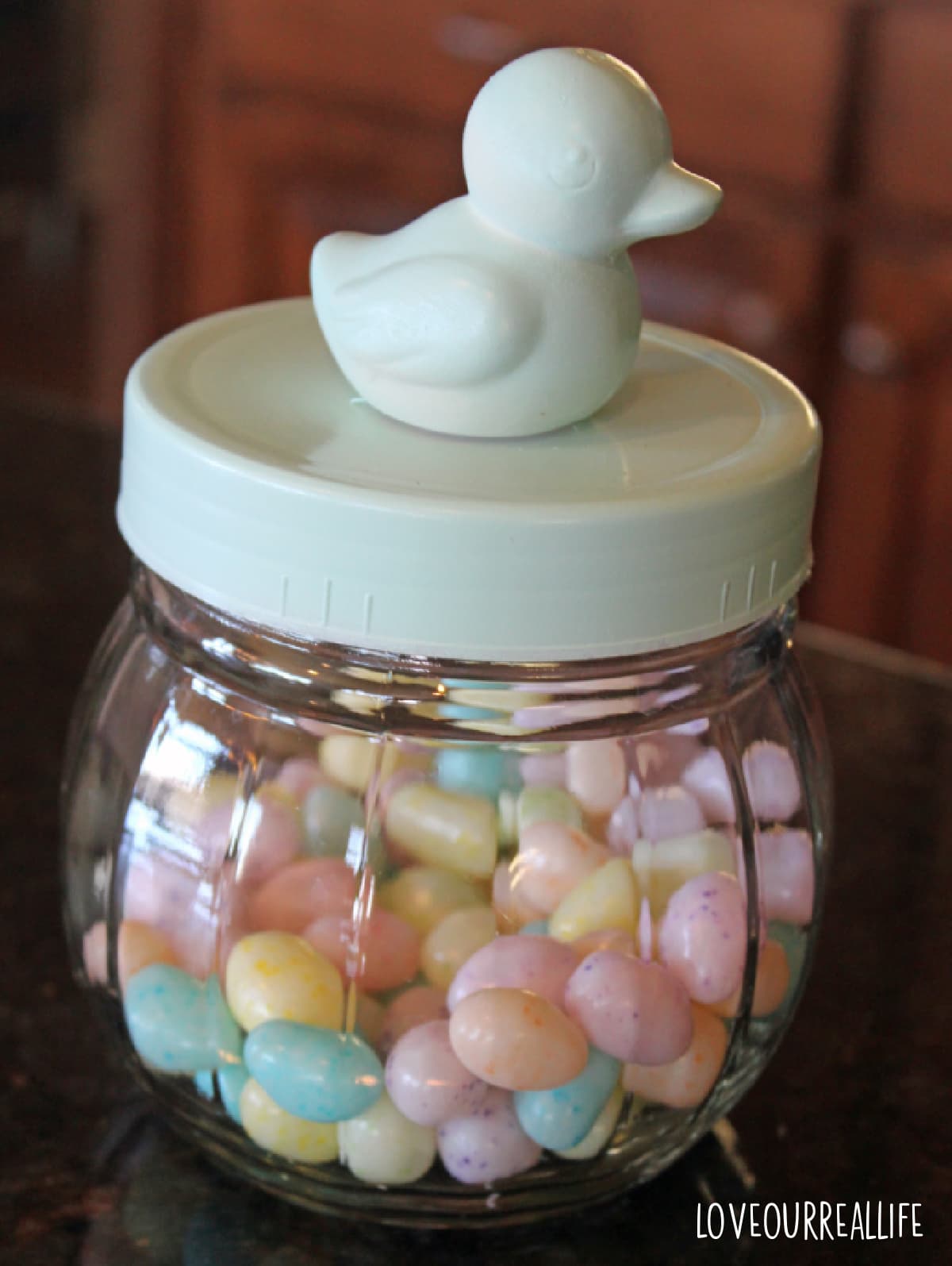 Glass jar with duck on top filled with pastel jelly beans.