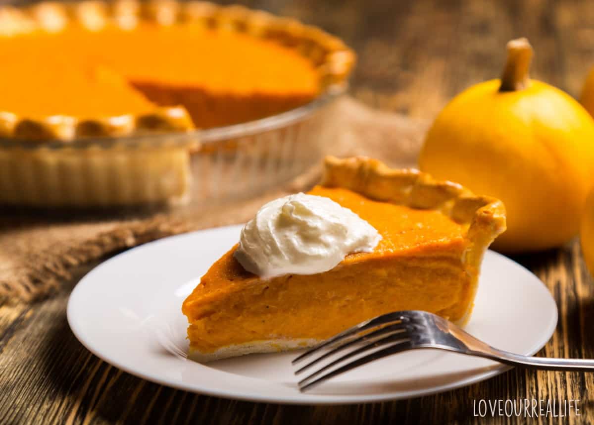 Pumpkin pie on white plate with fork with whole pie in background.