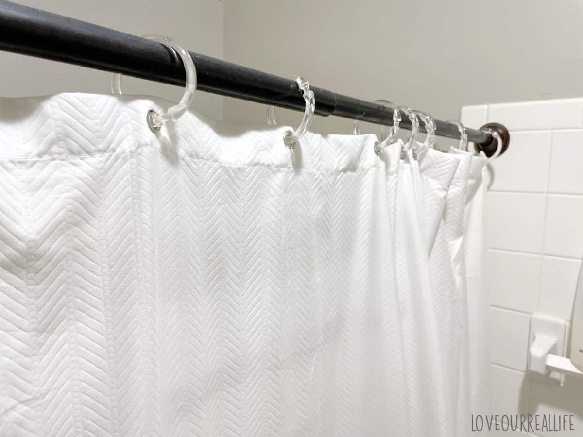 White cloth shower curtain liner hanging on black metal shower curtain rod.