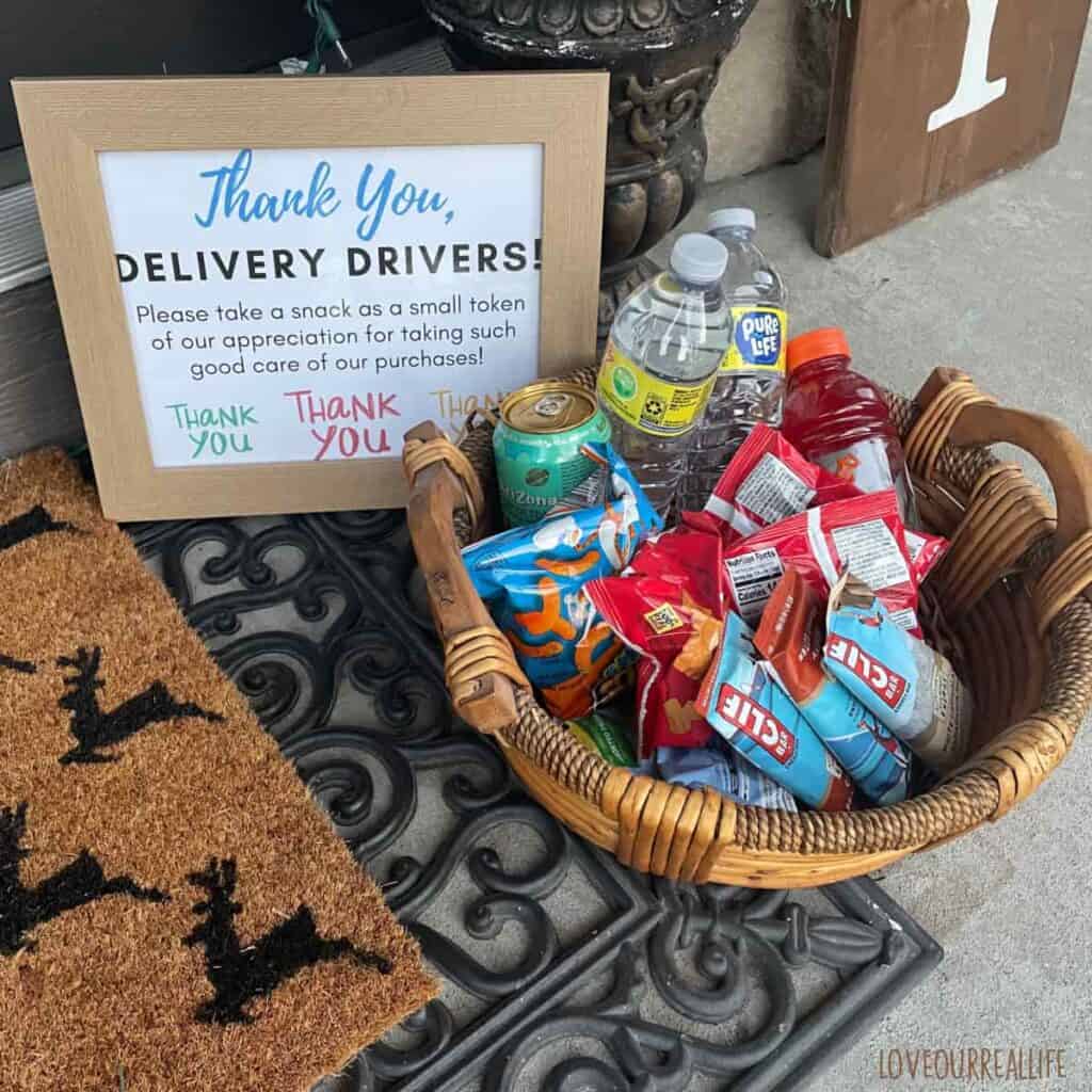 Thank you sign for delivery drivers beside wicker basket full of snacks on front porch.