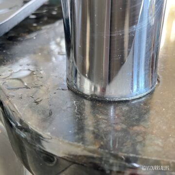 Water droplets and hard water stains forming around faucet and on granite countertop.