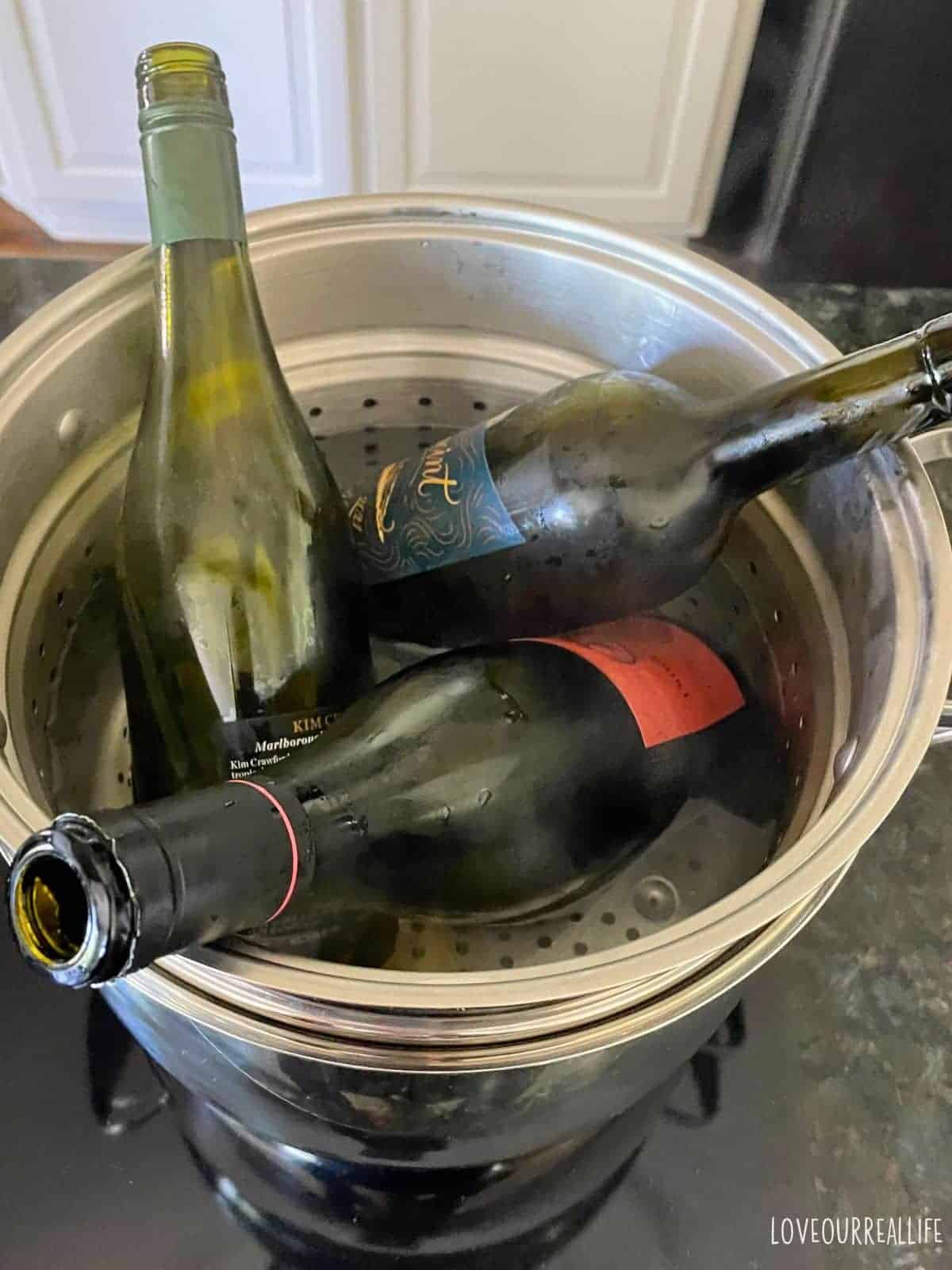 Wine bottles sitting in double boiler on stove top.
